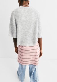 Grauer, flauschiger Strickpullover mit weiten Ärmeln, über einem rosa gestreiften Rock getragen und kombiniert mit hellblauen weiten Jeans.
