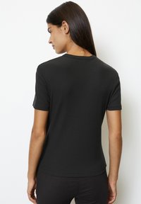 Camiseta ajustada negra de manga corta y cuello redondo. Elaborada en un material suave y con relieve, presenta una parte posterior lisa y bordes limpios.