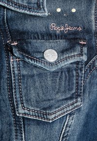 Denim jeans pocket with metal button and pink embroidered "Pepe Jeans" logo above, detailed stitching, and two metal rivets.