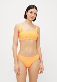 Svijetla narančasta bikini kombinacija koja se sastoji od kvadratnog bandeau gornjeg dijela sa širokim trakama i odgovarajućih donjih dijelova niskog struka. Glatka, rastezljiva tkanina.