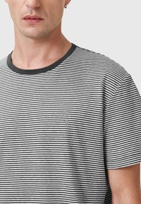 Stribet t-shirt i sort og hvid med rund hals. Har struktureret stof og et lille emblem på venstre bryst. Kortærmet.