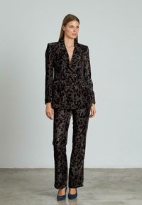 Completo in stampa leopardata in tonalità scure, con giacca doppiopetto e pantaloni aderenti. Texture in velluto con finitura lucida e dettagli a bottoni.