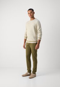 Lys beige strukturert genser med ribbestrikket hals, parret med mørk olivengrønne smale bukser. Beige slip-on sko fullfører antrekket.