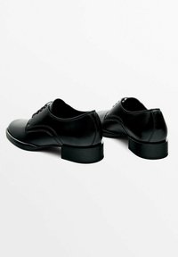 Pari kiilloitettuja mustia nahkakenkiä miesten juhlakengät matalilla koroilla ja nauhoilla, sijoitettu yksinkertaiselle valkoiselle taustalle.