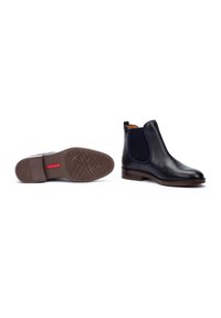 Bottines noires en cuir avec des panneaux élastiques sur les côtés et un petit talon. Comprend une semelle en caoutchouc marron avec un motif texturé et un accent rouge.