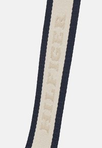 Laivastonsininen ja kerma värinen tekstiiliranneke, jossa kohopainettu "HILFIGER"-logo. Rannekkeessa on poimutettu rakenne ja sileä keskiosa. Suorakulmainen muoto.