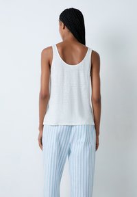 Top blanco sin mangas con un corte relajado, que presenta un escote redondeado en la parte posterior. Combinado con pantalones de pijama a rayas azul claro y blancos.