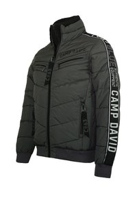 Dunkelgraue Steppjacke mit hohem Kragen, zwei Reißverschluss-Brusttaschen und Markenakzenten. Strukturierter Stoff mit gestepptem Design.