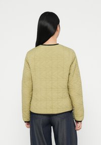 Quiltet jakke i olivengrøn med et geometrisk mønster, rund halsudskæring med sort kant og lange ærmer. Sættet er kombineret med mørk denimbukser.