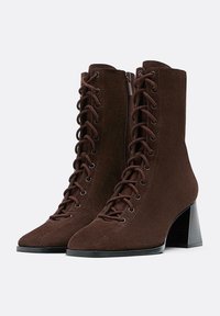 Stivaletti in suede marrone con finitura testurizzata, dotati di lacci anteriori, cerniere laterali e un tacco nero spesso.