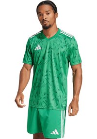 Grünes Sporttrikot mit subtilen dreieckigen Mustern, kurzen Ärmeln, V-Ausschnitt und weißen Streifen an den Schultern. Kombiniert mit passenden grünen Shorts.