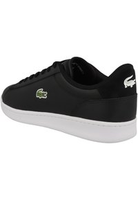 Svart syntetisk sneakers med en glatt overflate, hvit gummi såle og grønn og hvit krokodillelogo på siden. Snøring.