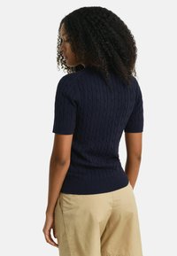 Suéter de punto cableado de manga corta en azul marino con un diseño ajustado, cuello y dobladillo acanalados. Combinado con pantalones cortos de un beige claro.