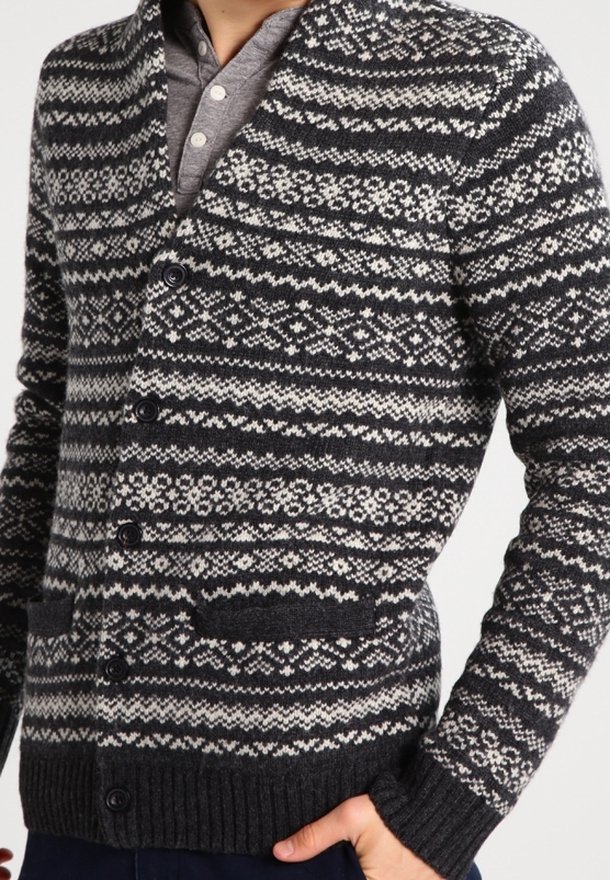 Cárdigan de punto en gris oscuro con patrones geométricos blancos. Cuenta con cuello chal, cierre de botones y dos bolsillos frontales. Puños acanalados texturizados.