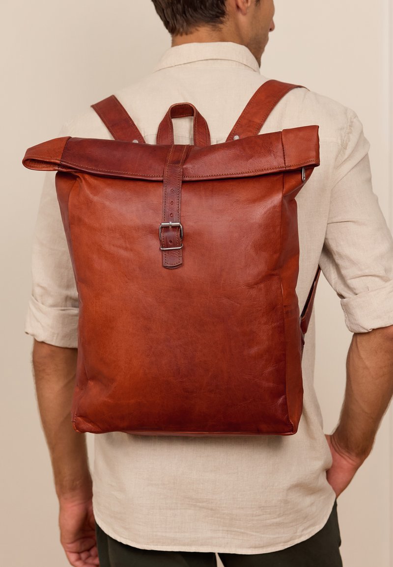 Brauner Lederrucksack mit Roll-Top-Design, verstellbaren Riemen und einer Metallschnalle, mit glatter Textur und minimalem Beschlag.
