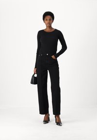 Langarmige, geribbelde zwarte top gecombineerd met hoge taille zwarte wijde jeans. Draagt het met zwarte lakleren hakken en een kleine zwarte handtas.