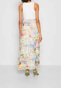 Robe maxi avec un haut blanc et un bas coloré illustré représentant des scènes de nature et d'architecture. Tissu fluide avec un design à volants.