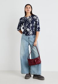 Marinebluse mit Blumenmuster und Puffärmeln, hellblaue Schlagjeans, kastanienbraune Schultertasche und graue Plateau-Stiefel.