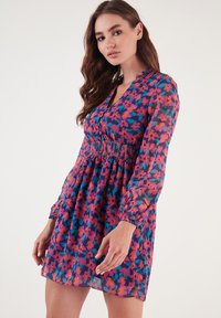 Blumenkleid mit langen, Ballonärmeln, einer gerafften Taille und mehrfarbigen Blumen auf blauem Hintergrund. Hergestellt aus leichtem Material.