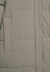 Giacca imbottita grigia con una texture liscia e lucida, chiusura con bottoni a pressione e tasca laterale dal design rettangolare.