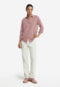 Långärmad, ljusrosa skjorta med knappar i ett mjukt material, i kombination med vita byxor och ljusrosa sneakers med gröna detaljer.