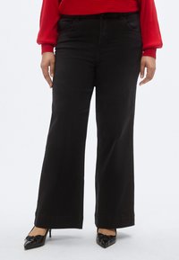 Jeans negri cu picioare largi, cu textură netedă, talie înaltă și accente cusute. Combinați cu balerini negri cu vârf ascuțit și un top roșu cu dungi.