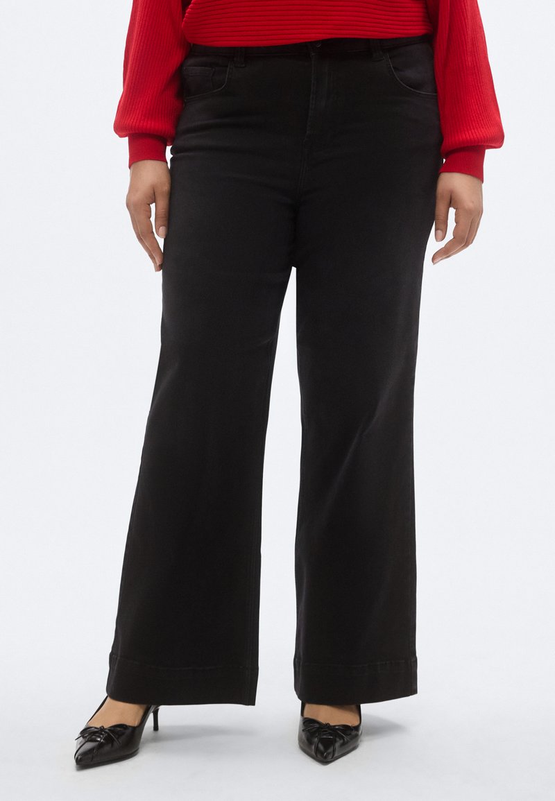 Jeans negri cu picioare largi, cu textură netedă, talie înaltă și accente cusute. Combinați cu balerini negri cu vârf ascuțit și un top roșu cu dungi.