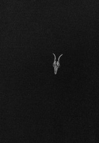 Schwarzes Strickoberteil mit einem kleinen, grau gestickten Ziegenschädel-Design auf der linken Seite. Glatte Textur mit einem einheitlichen Muster.