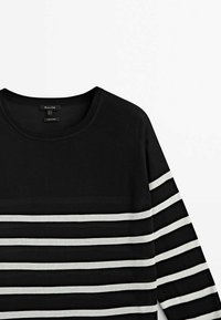 Chemise noire à manches longues avec des rayures horizontales blanches sur les manches et le bas de la poitrine, dotée d'un col rond et d'un col côtelé.