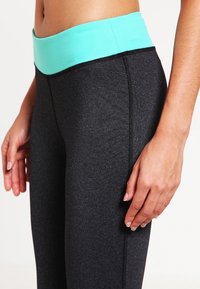 Leggings sportivi neri con una fascia in verde menta, caratterizzati da una texture liscia e cuciture a contrasto lungo le cuciture.