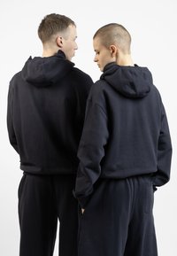 Black hooded sweatshirts with a soft texture, featuring a relaxed fit and kangaroo pockets, paired with matching dark pants.