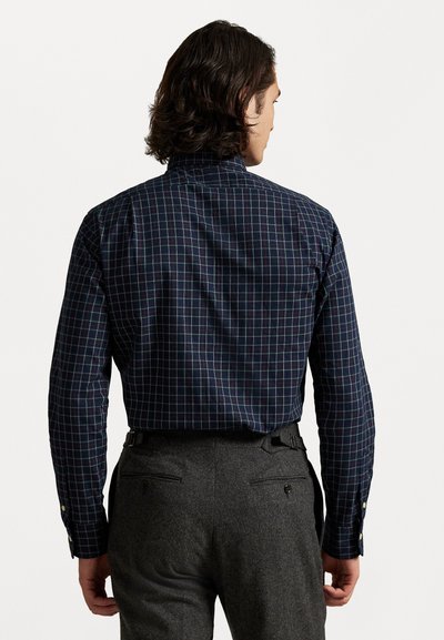 Langermet marineblå skjorte med flerfargede rutemønster, knappede mansjetter og klassisk krage; brukt med grå bukser med baklommer.