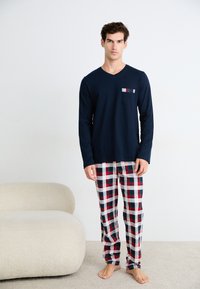 Camicia a maniche lunghe di colore blu navy con una tasca sul petto; abbinata a pantaloni a scacchi nei colori rosso, verde e bianco. Tessuto morbido, stile casual per il tempo libero.