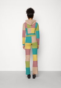 Ensemble coloré en deux pièces composé d'un hoodie cropped et de pantalons évasés, fabriqué en tissu rayé et à carreaux dans les tons de vert, rose, bleu et jaune.