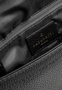Interno di una borsa in pelle nera con rivestimento in tessuto liscio, chiusura con zip e doppia cucitura, e un'etichetta in pelle nera con logo.