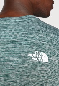 Roheline, tekstureeritud lühikeste varrukatega särk ümarate kraega. Selja ülaosas on valge logo "THE NORTH FACE".
