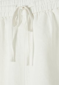 Linen white trousers with an elastic waistband and drawstring. The fabric has a slightly textured surface, providing a relaxed fit.