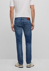Blå denimjeans med rak benform, med bakfickor och en brun läderetikett med texten "BOSS" nära midjan.