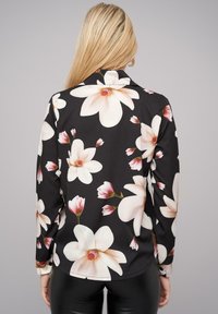 Lange mouwen blouse met een zwarte achtergrond, voorzien van grote witte en roze bloemenpatronen. Glad stof met een kraag en knoopdetails.