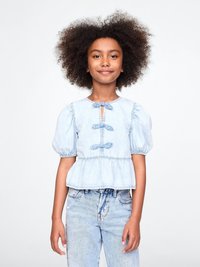 Lyseblå denimbluse med korte puffermer, nøkkelhullslukking foran og volangkant. Kombinert med lyseblå høyhårede jeans.