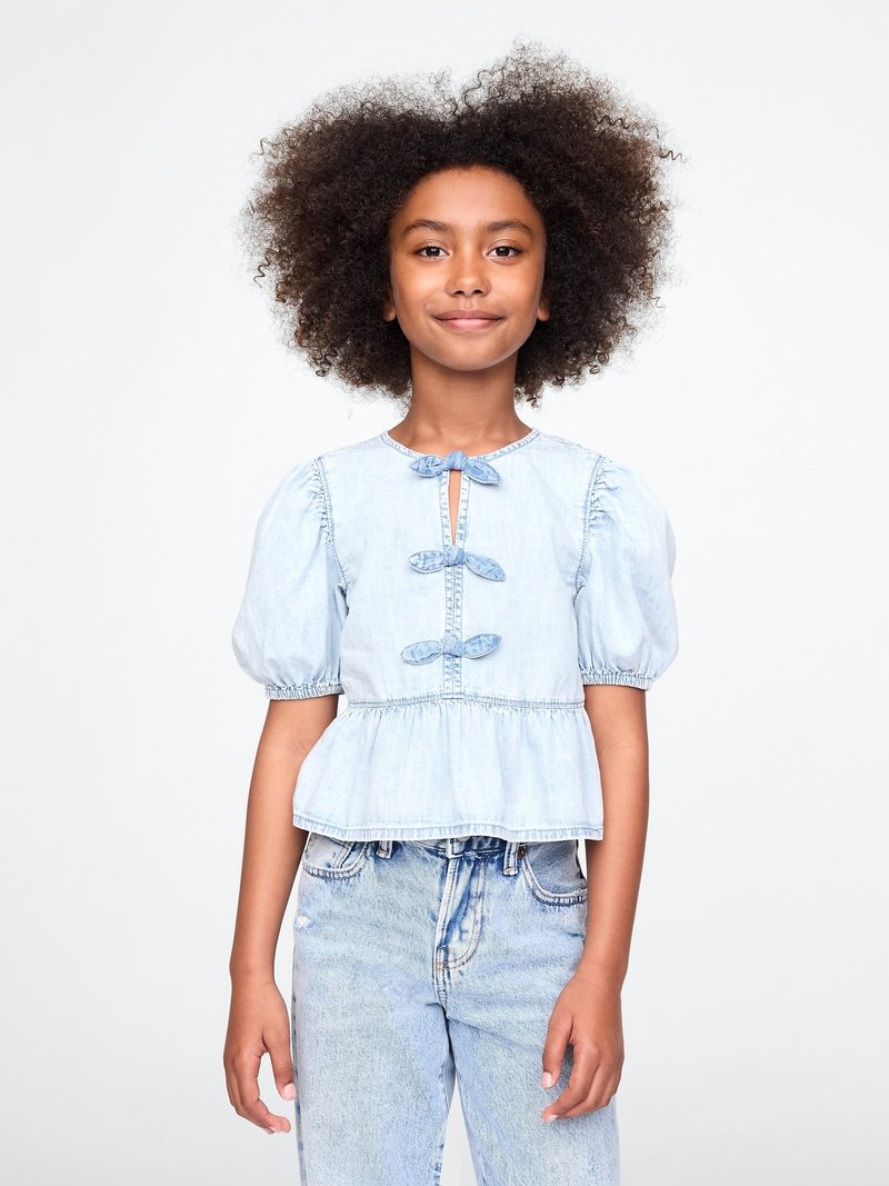 Lyseblå denimbluse med korte puffermer, nøkkelhullslukking foran og volangkant. Kombinert med lyseblå høyhårede jeans.