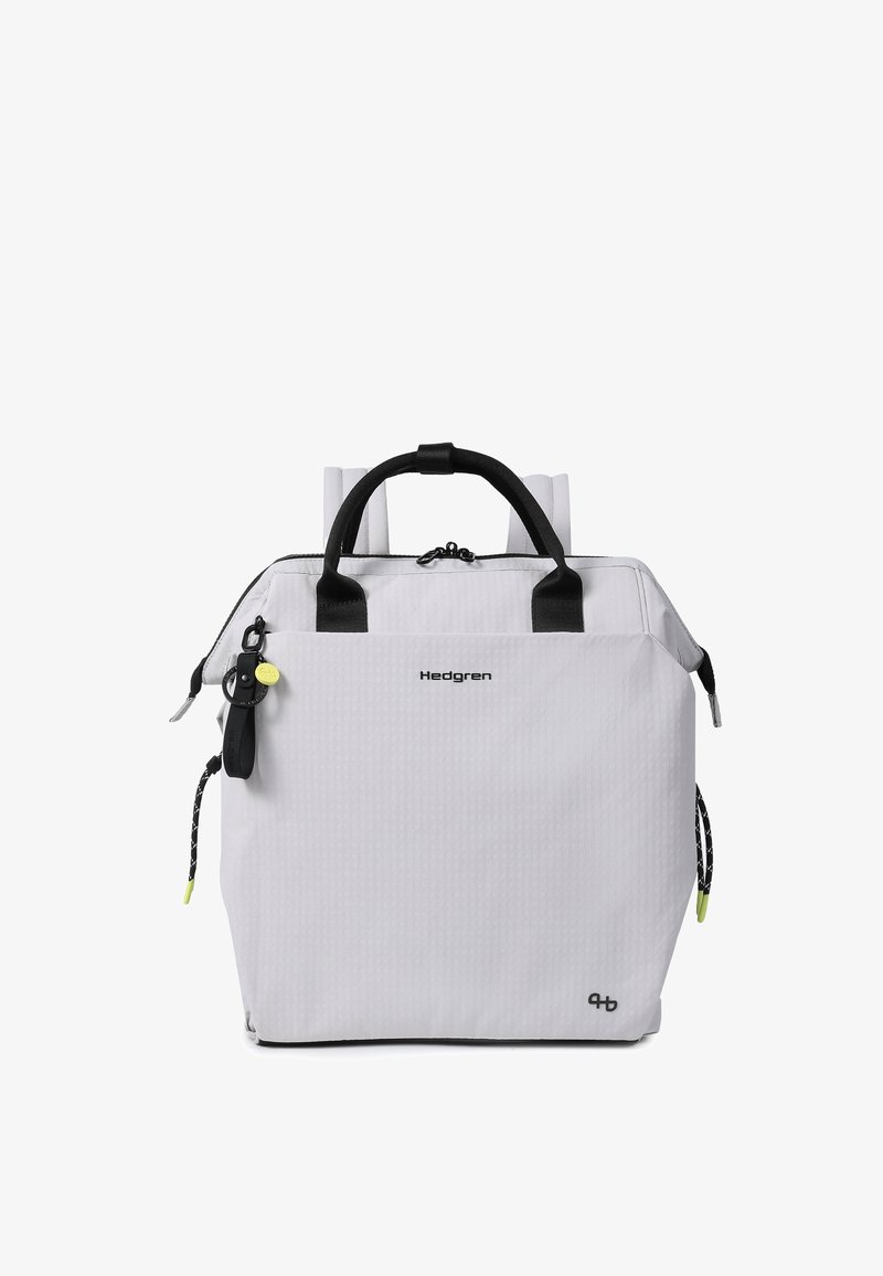 Sac à dos blanc Hedgren avec poignées noires, bretelles, poche avant zippée et porte-clés noir attaché avec une étiquette jaune.
