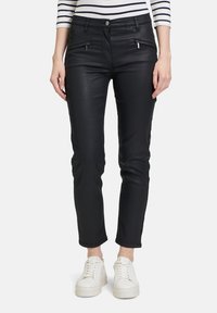 Schwarze Slim-Fit-Hosen aus einem glänzenden Material, ausgestattet mit Taschen mit Reißverschluss und einem Knopfverschluss, kombiniert mit weißen Sneakern.