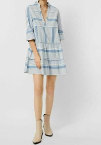 Sininen ja valkoinen raidallinen mekko, jossa on v-pääntie, kolmannes hihasta ja kerroksellinen hame. Yhdistetty vaaleanbeigeihin nilkkabootseihin.