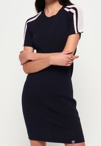 Abito in maglia navy con maniche corte, caratterizzato da accenti in rete rosa sulle spalle. Design aderente, texture a coste e logo del brand sull'orlo.