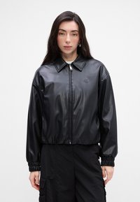 Giacca bomber nera in pelle sintetica con chiusura a zip, colletto a punta e polsini elasticizzati. Presenta un dettaglio logo sul petto.