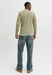 Pull texturé kaki avec un col ajusté, associé à un jean bleu clair à coupe ample. Des chaussures beiges à semelles en caoutchouc complètent la tenue.