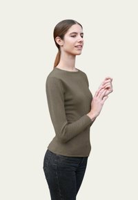 Haut à manches longues de couleur olive, fabriqué dans un tissu doux, design ajusté, col rond, associé à un jean noir, créant une silhouette élégante.