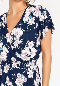 Květinové šaty s obalem v námořnické modři s bílými a růžovými květy. Mají řasené rukávy a elastický pas, který zdůrazňuje měkkou, lehkou látku.