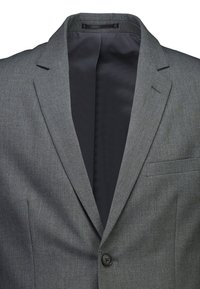 Grijs herenjasje met één zwarte knoop, opstaand revers, borstzak en zwarte voering.